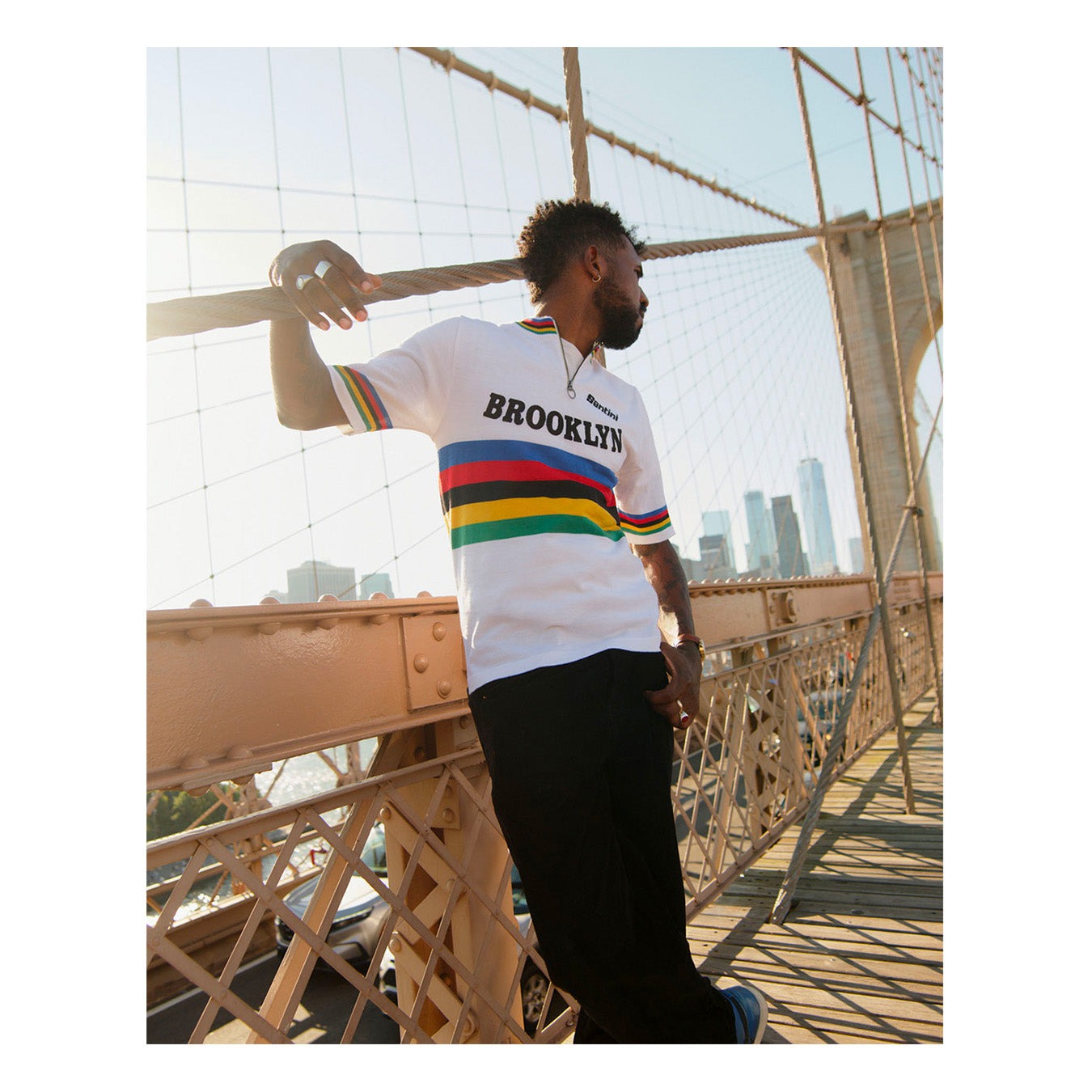 Een man in een witte Brooklyn-retrotrui met regenboogstrepen op de Brooklyn Bridge in New York
