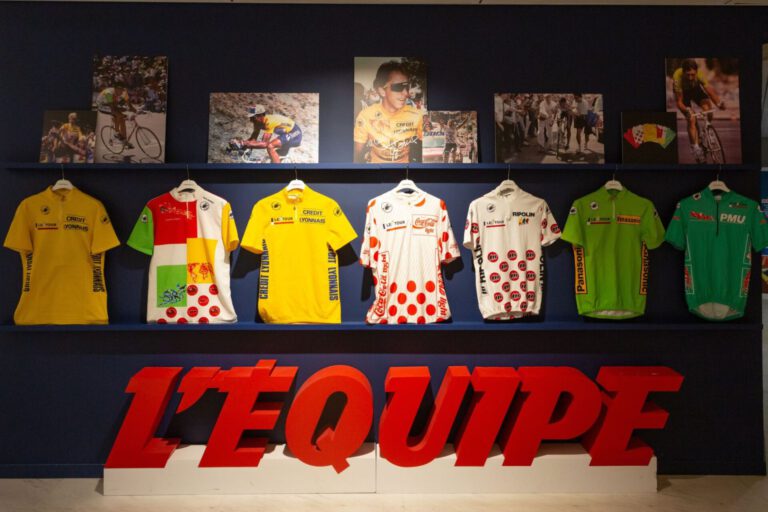 Castelli-truien uit de Tour de France van 1989 tot 1994, met gele, bolletjes-, groene en witte truien, aan een wand bij L'Équipe