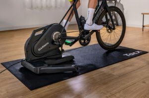 Racefiets op de Garmin Tacx Nēra smart trainer op een zwarte Tacx-mat in een woonkamer met houten vloer