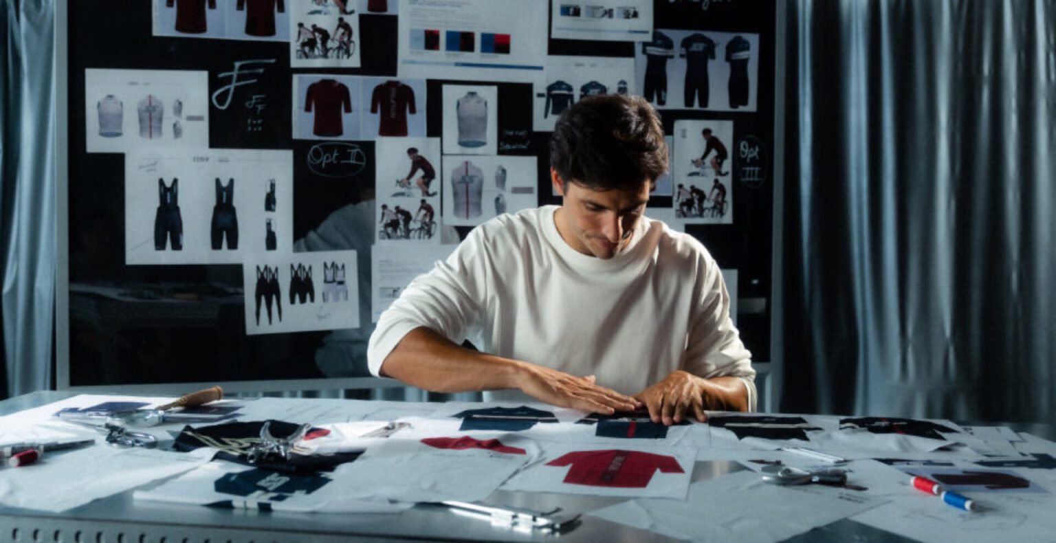 Carlos Sainz aan een ontwerptafel met stofstalen en wielershirts bij Gobik