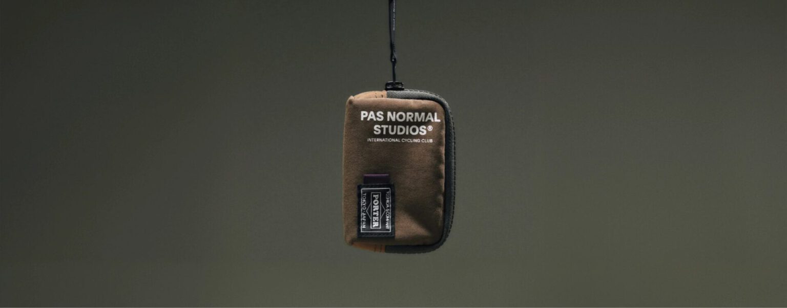 Bruin etui van Pas Normal Studios x Porter aan een koord tegen een donkergroene achtergrond
