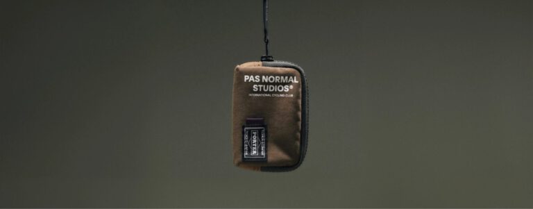 Bruin etui van Pas Normal Studios x Porter aan een koord tegen een donkergroene achtergrond